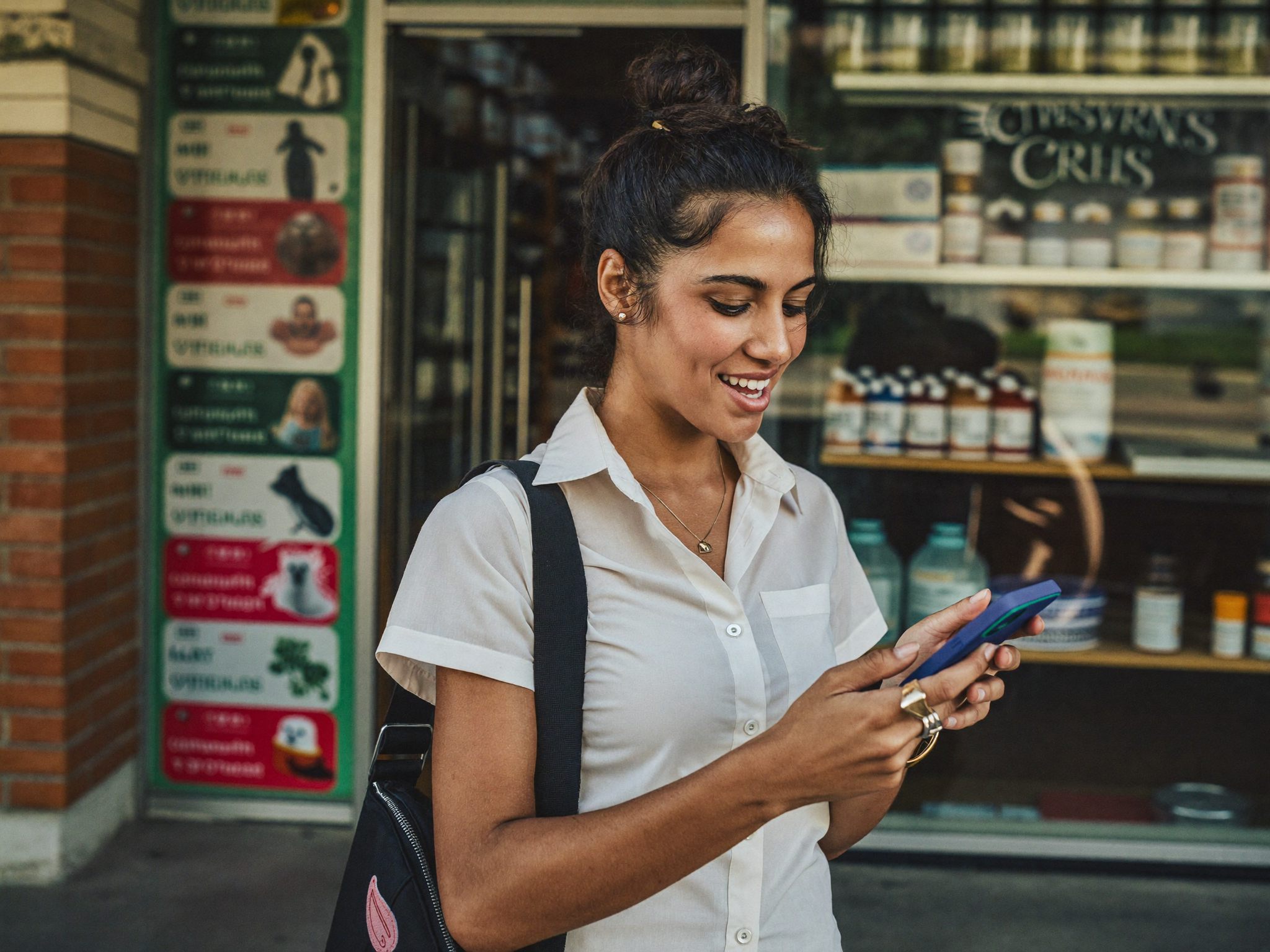 Jovem empreendedora usando o celular em frente à sua loja para registrar o negócio